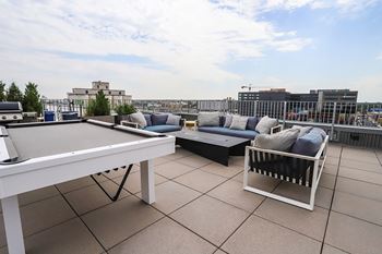 A white table and a sofa with cushions are on a rooftop patio.